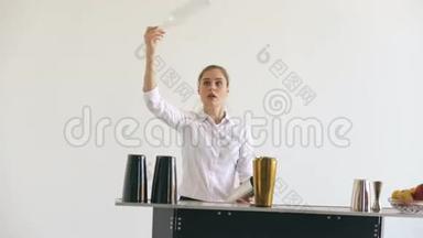专业调酒师女孩在白色背景工作室的移动酒吧桌上摆弄瓶子和摇动鸡尾酒